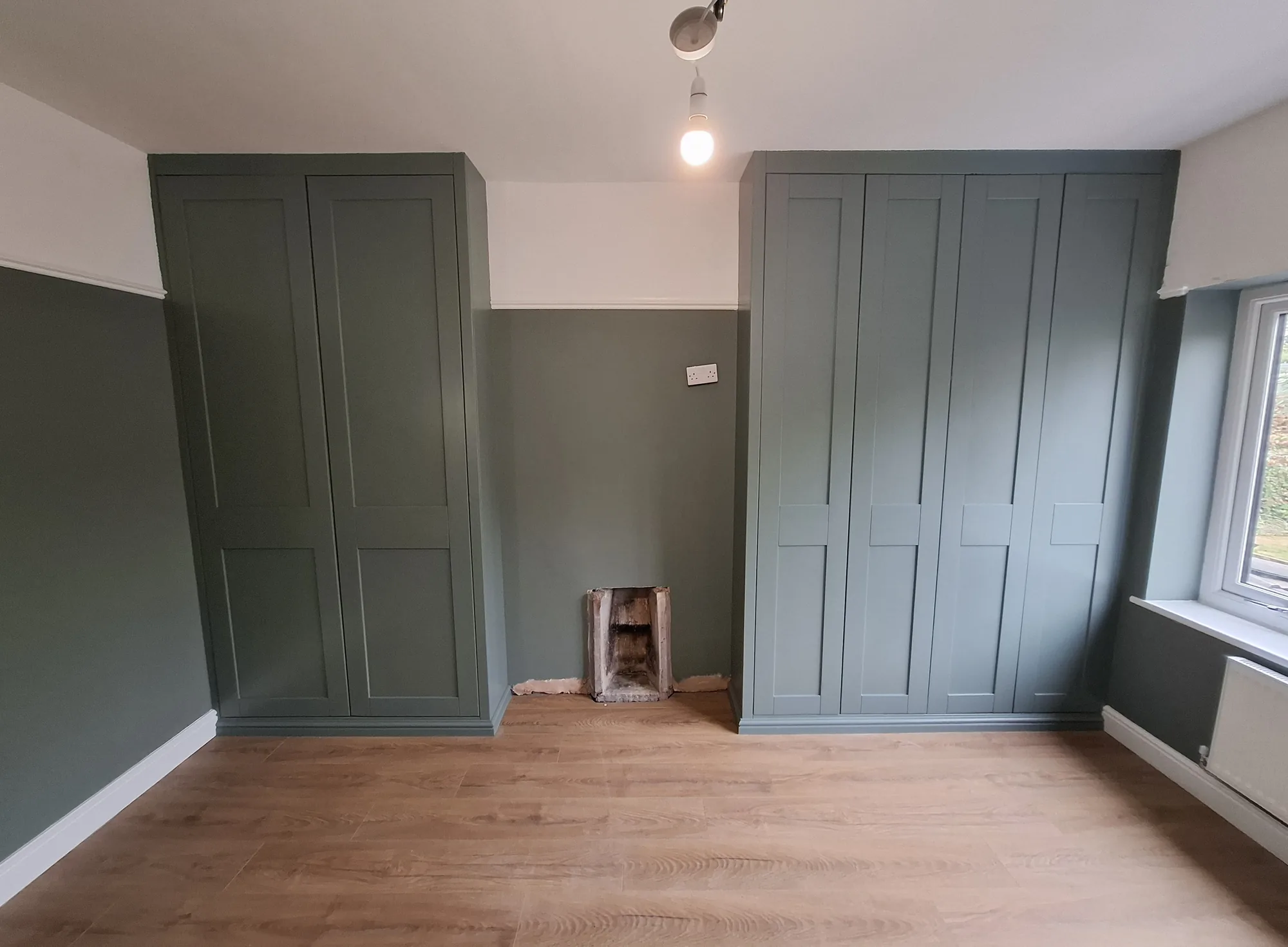Green shaker wardrobes either side of a chimney breast